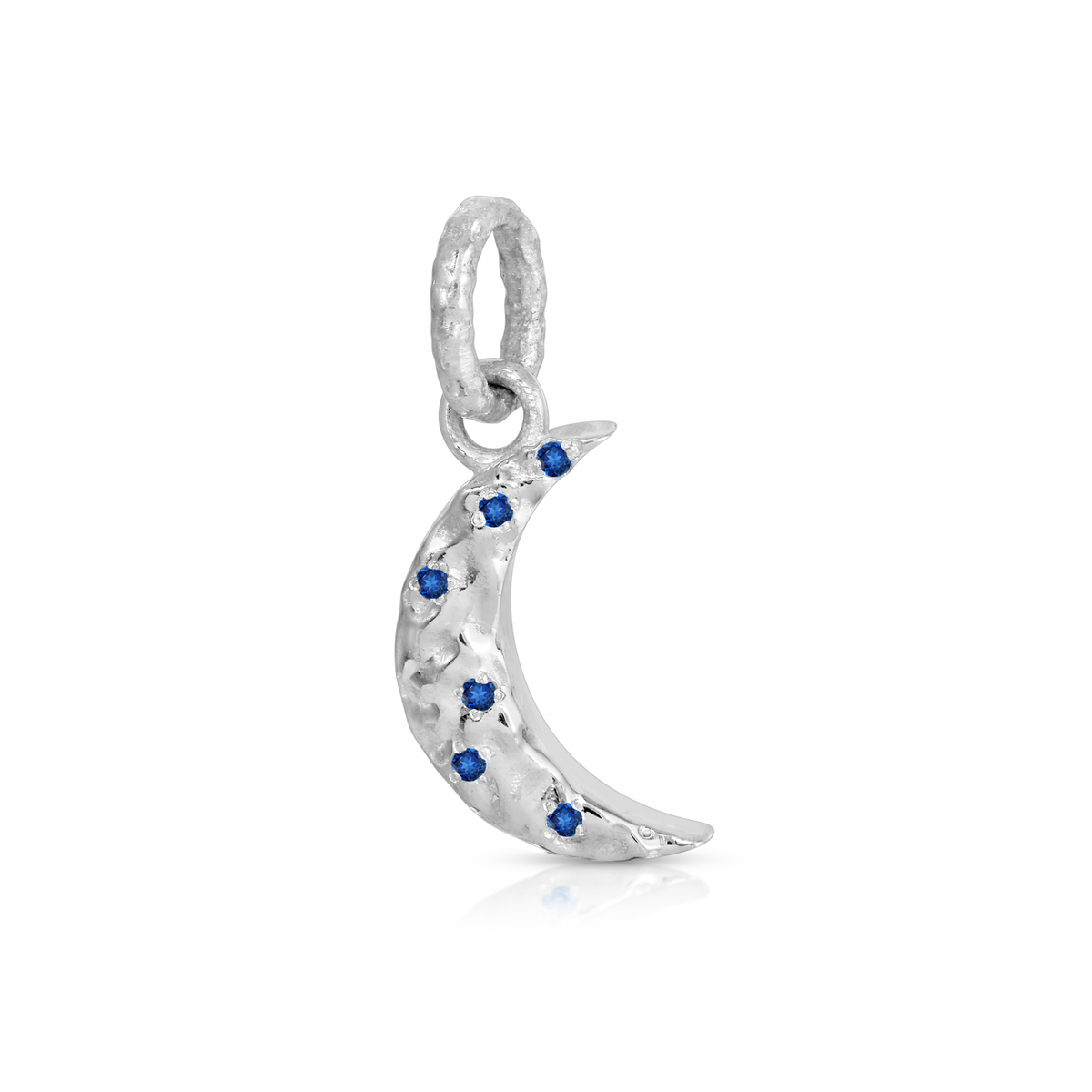 A silver crescent moon charm embellished with small blue gemstones, shown on a clean white background with a soft reflection.
